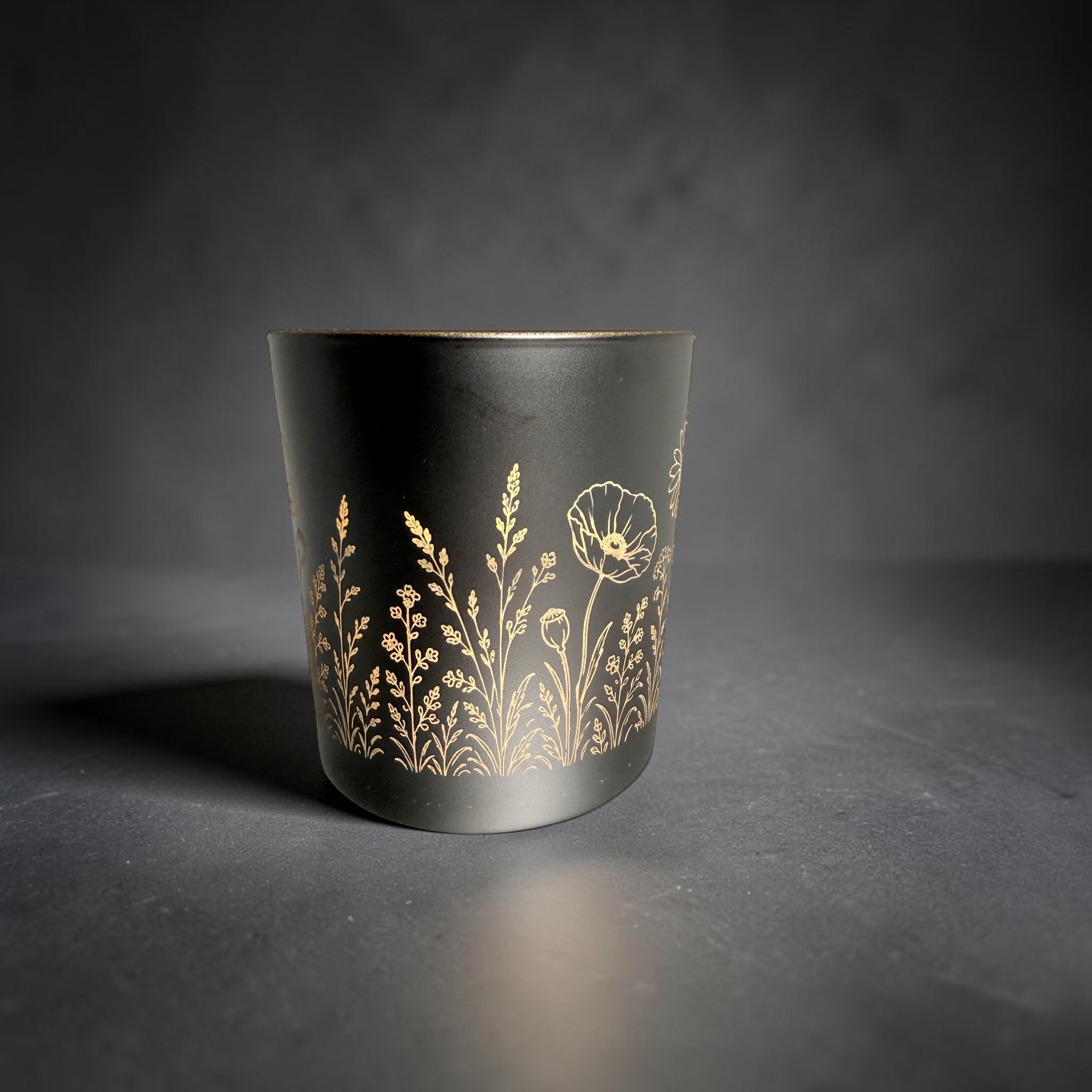 [Laser cut and engrave] Black candle holder with gold interior, engraved all around with a delicate wildflower meadow design using a rotary laser setup.