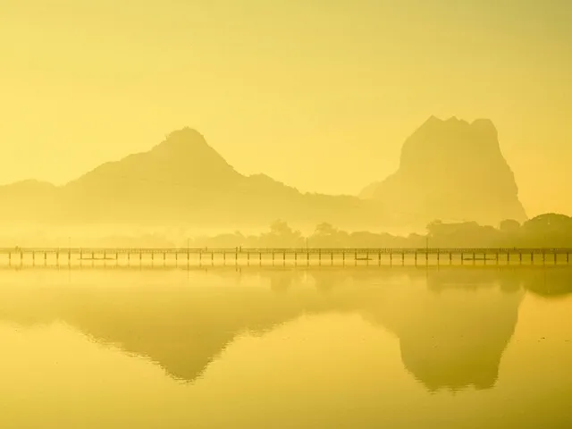 Golden sunrise landscape with a long wooden bridge over a calm lake